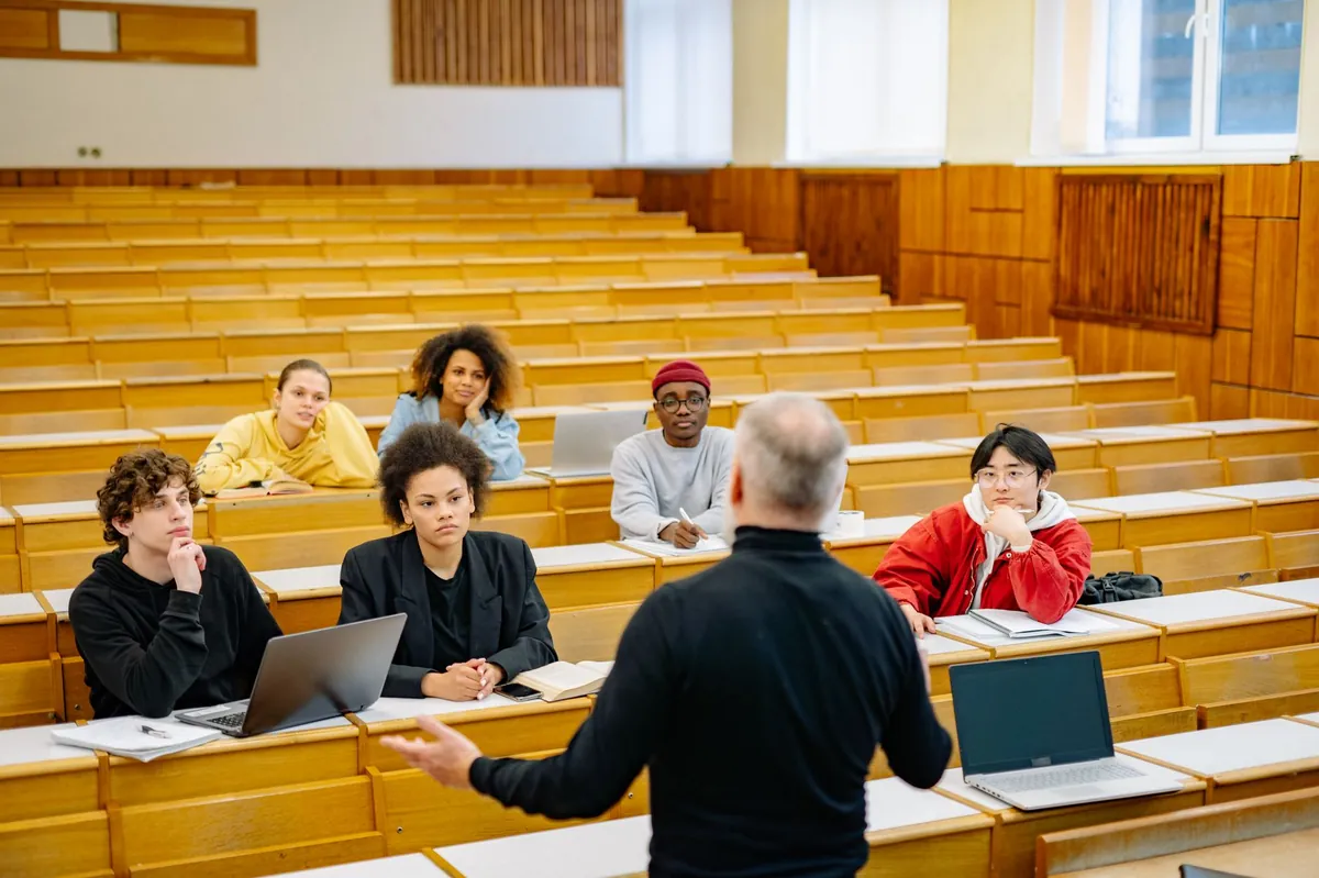 A professor lectures to a diverse group of students seated in a tiered university lecture hall.