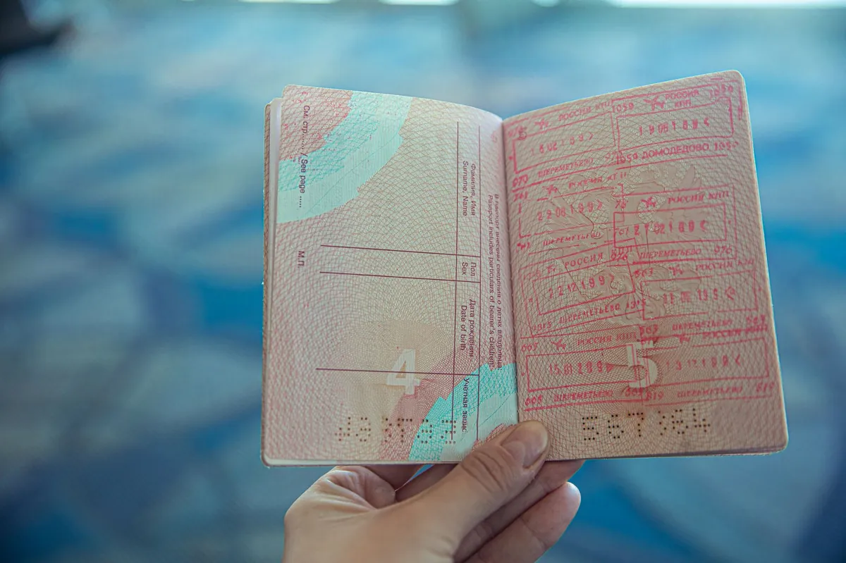 An open passport with multiple colorful travel stamps and entry marks, viewed up close in a bright airport terminal with soft-focus background activity.
